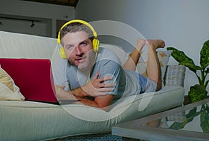 Young attractive and happy man with headphones at home sofa couch relaxed smiling cheerful using internet on laptop computer worki