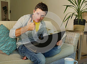 Young attractive and happy man at home relaxed working on laptop computer sitting at living room sofa couch smiling cheerful as in