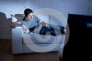 Young attractive happy man lying on couch at living room watching excited tv holding remote control