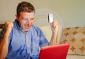 Young attractive and happy man relaxed at home sofa couch using credit card and laptop computer for internet shopping and banking