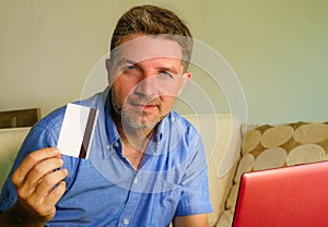 Young attractive and happy man relaxed at home sofa couch using credit card and laptop computer for internet shopping and banking