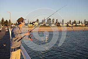 Young attractive and happy man in shirt and hat fishing at beach sea dock using fish road enjoying weekend hobby in holidays