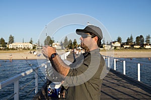 Young attractive and happy man in shirt and hat fishing at beach sea dock using fish road enjoying weekend hobby in holidays