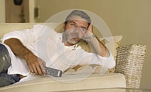 Young attractive and happy man watching television show or movie holding TV remote controller enjoying relaxed lying on living