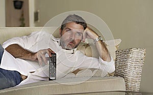 Young attractive and happy man watching television show or movie holding TV remote controller enjoying relaxed lying on living