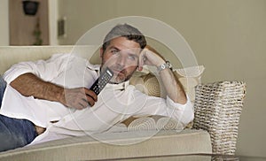 Young attractive and happy man watching television show or movie holding TV remote controller enjoying relaxed lying on living