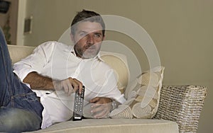 Young attractive and happy man watching television show or movie holding TV remote controller enjoying relaxed lying on living