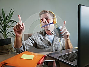 Young attractive and happy man with yellow headphones sitting at home office desk working with laptop computer having fun listenin