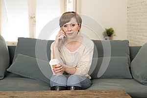 Young attractive and happy red hair woman sitting at home sofa couch drinking coffee talking on mobile phone relaxed in communicat