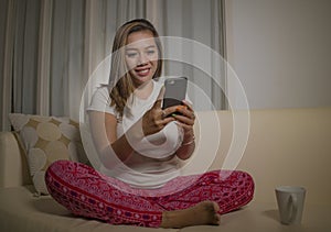 Young attractive happy and relaxed student girl enjoying homey sitting at living room sofa couch using internet social media or