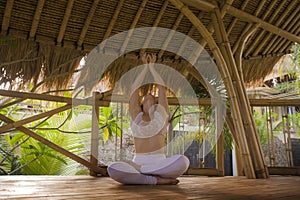 Young attractive and happy relaxed woman sitting in lotus yoga position doing meditation and concentration outdoors at wooden hut