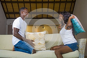 Young attractive and happy romantic African American couple in love playful at living room couch playing pillow fight enjoying