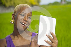 Young attractive and happy successful black afro american woman working with digital tablet pad outdoors on green field cafe smili