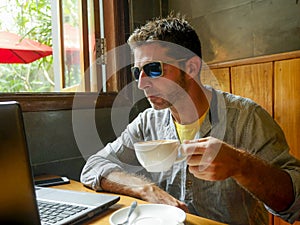 Young attractive happy and successful millennial man working from internet coffee shop with laptop computer and mobile phone relax