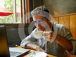 Young attractive happy and successful millennial man working from internet coffee shop with laptop computer and mobile phone relax