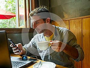 Young attractive happy and successful millennial man working from internet coffee shop with laptop computer and mobile phone relax