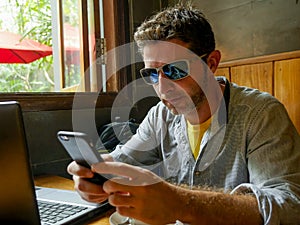 Young attractive happy and successful millennial man working from internet coffee shop with laptop computer and mobile phone relax