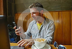 Young attractive happy and successful millennial man working from internet coffee shop with laptop computer and mobile phone relax