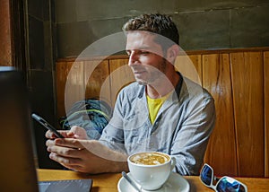 Young attractive happy and successful millennial man working from internet coffee shop with laptop computer and mobile phone relax