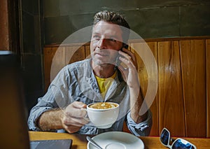 Young attractive happy and successful millennial man working from internet coffee shop with laptop computer talking on mobile phon