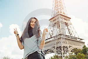 Young attractive happy woman showing peace gesture Eiffel Tower in Paris, France