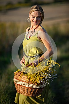 A young attractive herbalist holds a wicker basket of herbs. Goldenrod and common winterflower.