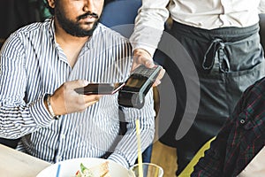 Young attractive Hindu man paying in cafe with contactless smartphone payment