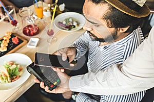 Young attractive Hindu man paying in cafe with contactless smartphone payment