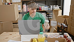 Young, attractive hispanic man volunteering at charity center, diligently checking product donations on laptop while sitting