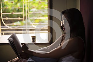 Young Indian brunette woman in white sleeping wear reading book on a bed