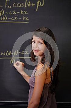 Showing her methodology. A young attractive Indian woman, solving a maths problem on the blackboard in class.