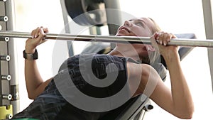 Young attractive lady working out in the gym - lifting barbell - chest muscles exercise