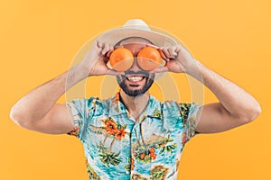 young attractive Latin American man laughing and putting oranges on eyes studio shot medium closeup orange background