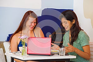 Young attractive latin girl sitting at modern cafe having lunch with happy woman as girlfriends meeting for discussing project in