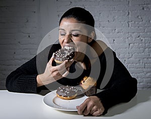 Young attractive latin woman sitting at table eating dish full of junk sugary unhealthy food