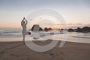Young attractive latin woman wearing a bikini practicing hands up yoga on the beach at sunset, healthy lifestyle concept