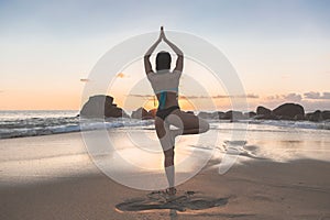Young attractive latin woman wearing a bikini practicing yoga on the beach at sunset, healthy lifestyle concept