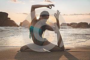 Young attractive latin woman wearing a bikini practicing yoga on the beach at sunset, healthy mental and body lifestyle concept