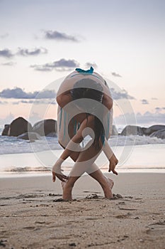 Young attractive latin woman wearing a bikini practicing yoga on the beach at sunset, healthy mental and body lifestyle concept