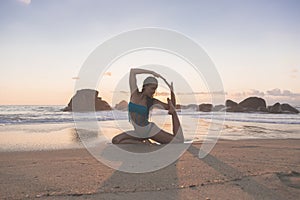 Young attractive latin woman wearing a bikini practicing yoga on the beach at sunset, healthy mental and body lifestyle concept. Y