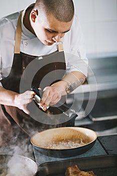 Young attractive male cook with uniform preparing delicious food.