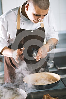 Young attractive male cook with uniform preparing a meat sause.