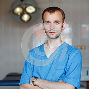 Young attractive male doctor in blue medical clothing is standing in the hospital in the operating room