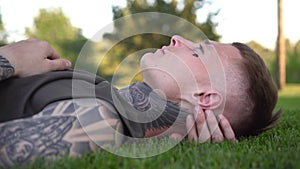 Young attractive male model lies on a green lawn in the park.