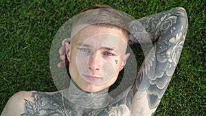 Young attractive male model with tattoos lies on the green grass in the park