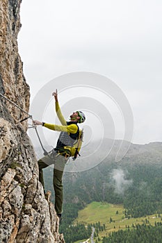 Young attractive male mountain climber in the Dolomites of italy pointing to the summit