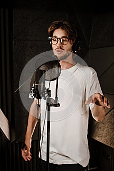Young attractive male musician in headphones intently recording song for new music album in sound studio