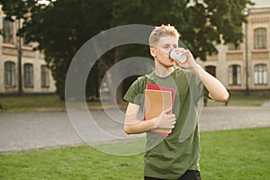 Young attractive male student holding notebooks and drinking take away coffee near the university. Handsome college student in the