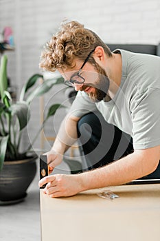 Young attractive man assembles furniture - handwerker and interior objects concept