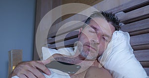 Young attractive man in bed sleeping tired and exhausted with mobile phone on his chest after networking in internet addiction and